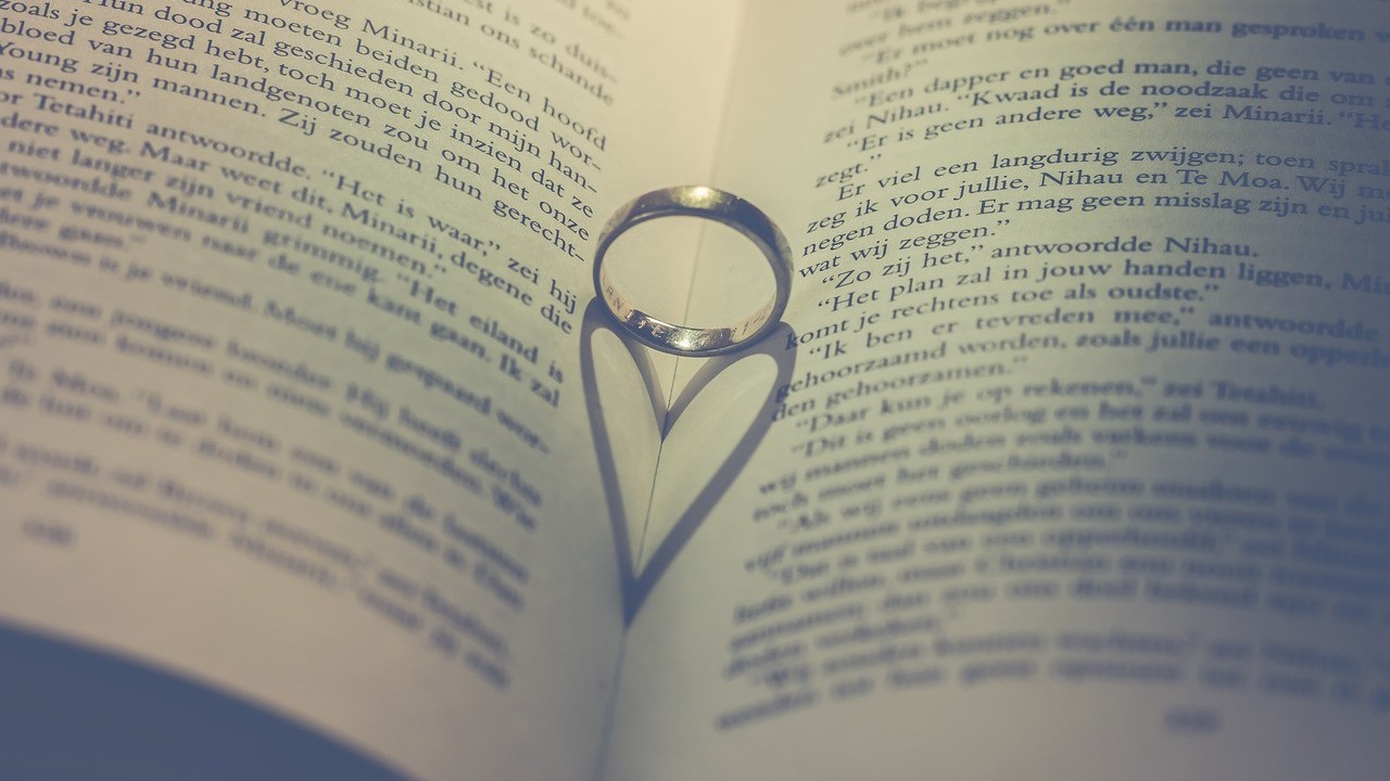 Aliança sobre um livro aberto, sombra em forma de coração